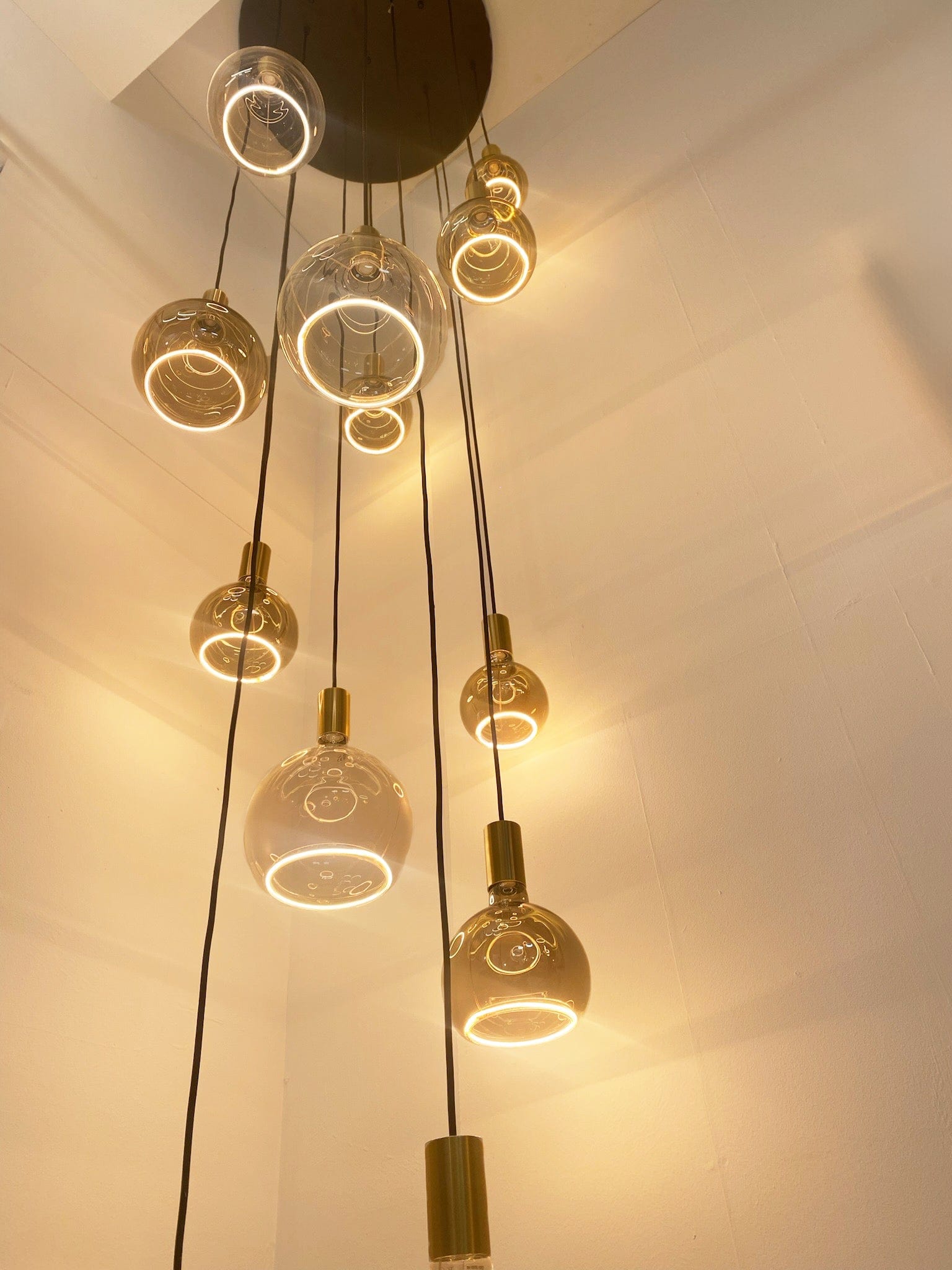 A ceiling-mounted pendant light fixture with multiple gold circular suspensions, some with a clear globe cover and others with a smoked cover, providing an elegant aesthetic.