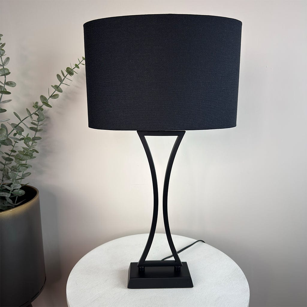 Black table lamp with a curved base on a white surface, next to a plant.