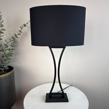 Black table lamp with a curved base on a white surface, next to a plant.