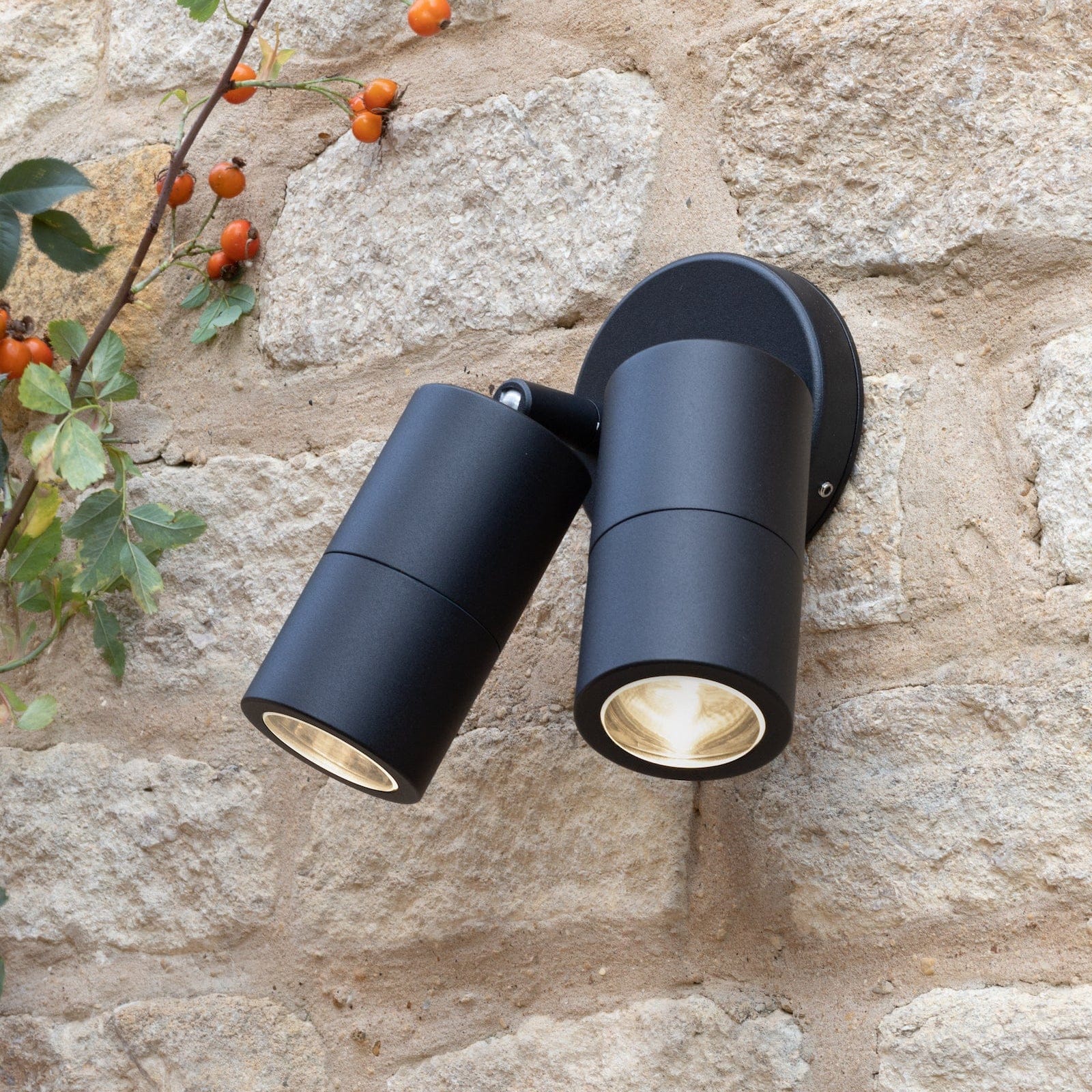 Black outdoor wall lights mounted on a stone wall with foliage.