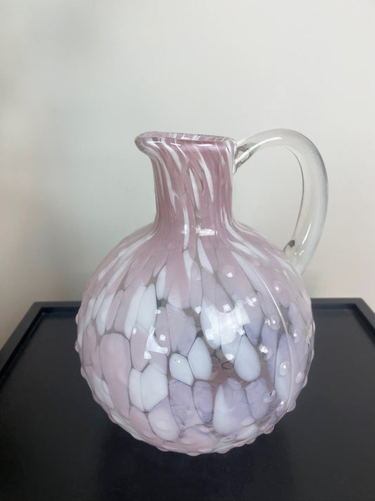Pink glass pitcher with white marbled pattern on a black surface