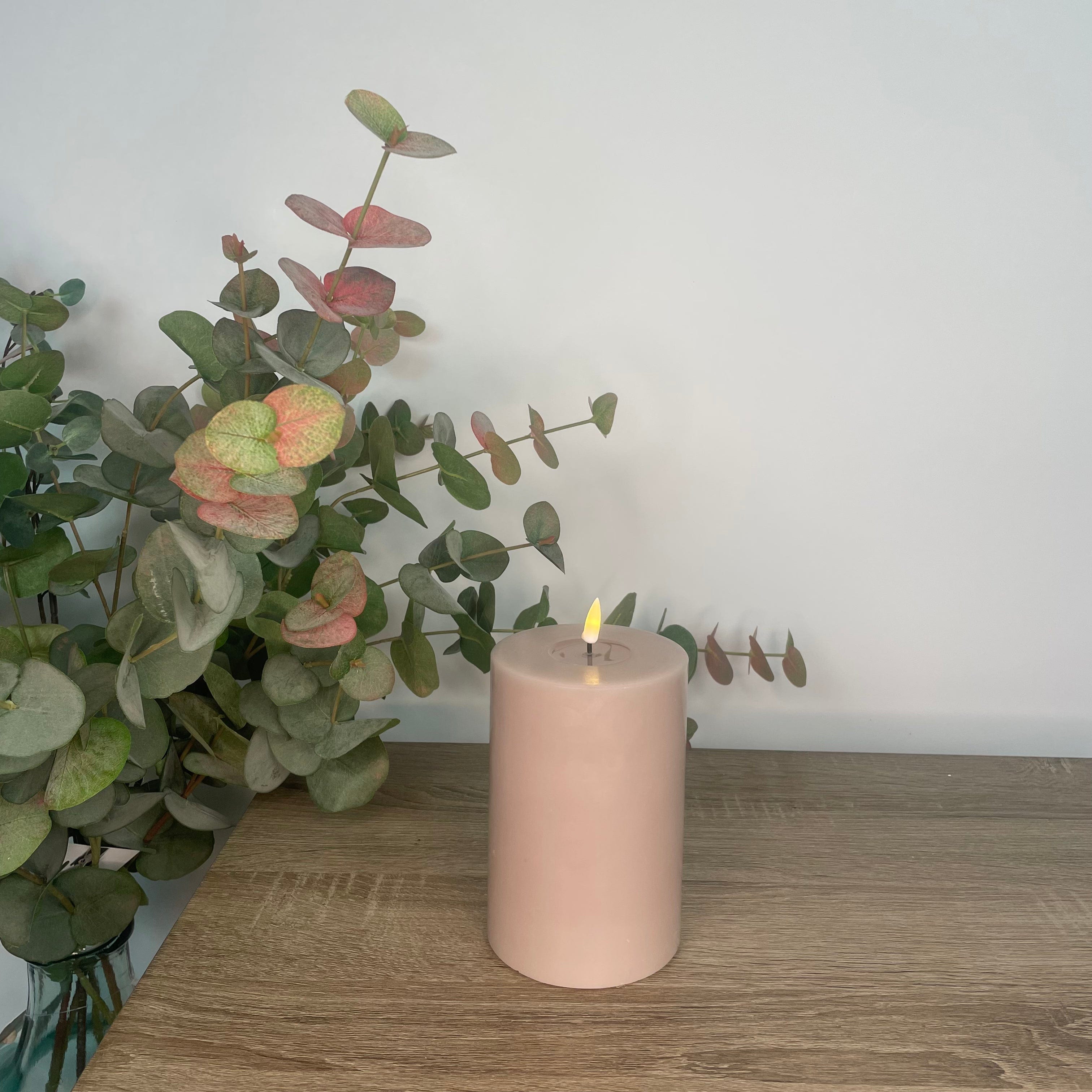 A pink LED candle placed on a wooden surface with a green plant in the background.