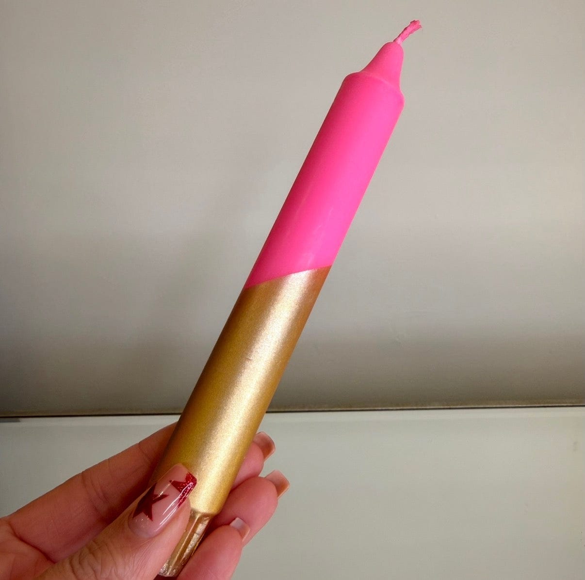 Pink and gold candle held by a hand against a plain background