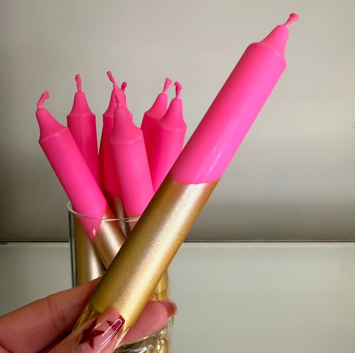 Pink candles with a gold holder held by a hand against a neutral background