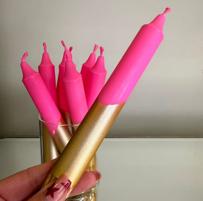 Pink candles with a gold holder held by a hand against a neutral background
