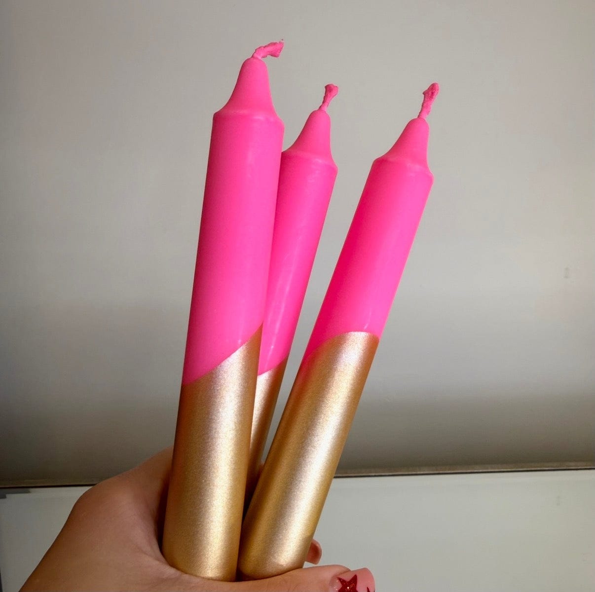 Three pink and gold candles held in a hand against a neutral background