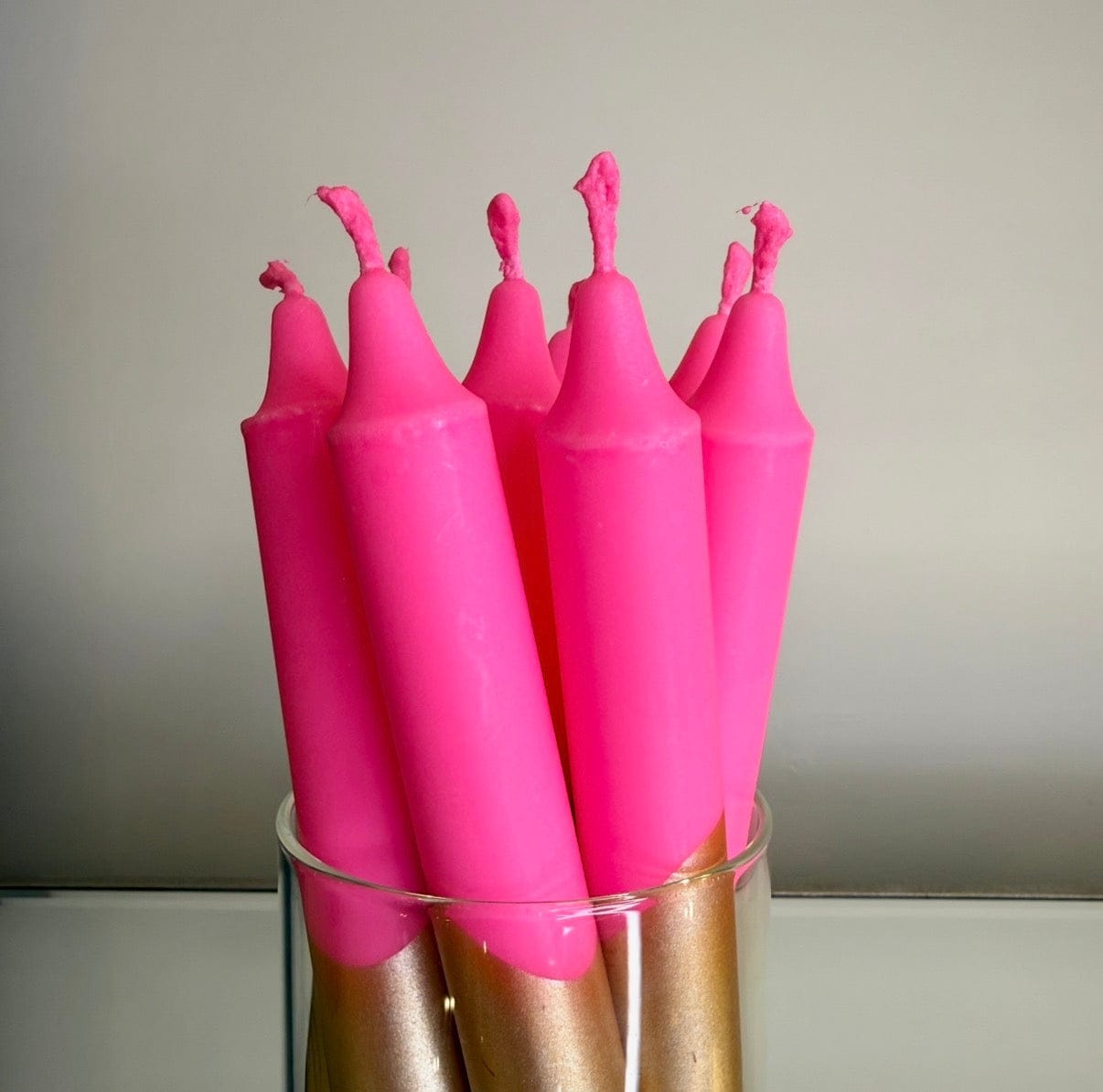 Pink candles with wicks in a clear glass holder against a neutral background