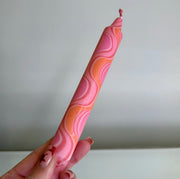 Hand holding a pink and orange patterned object against a plain background