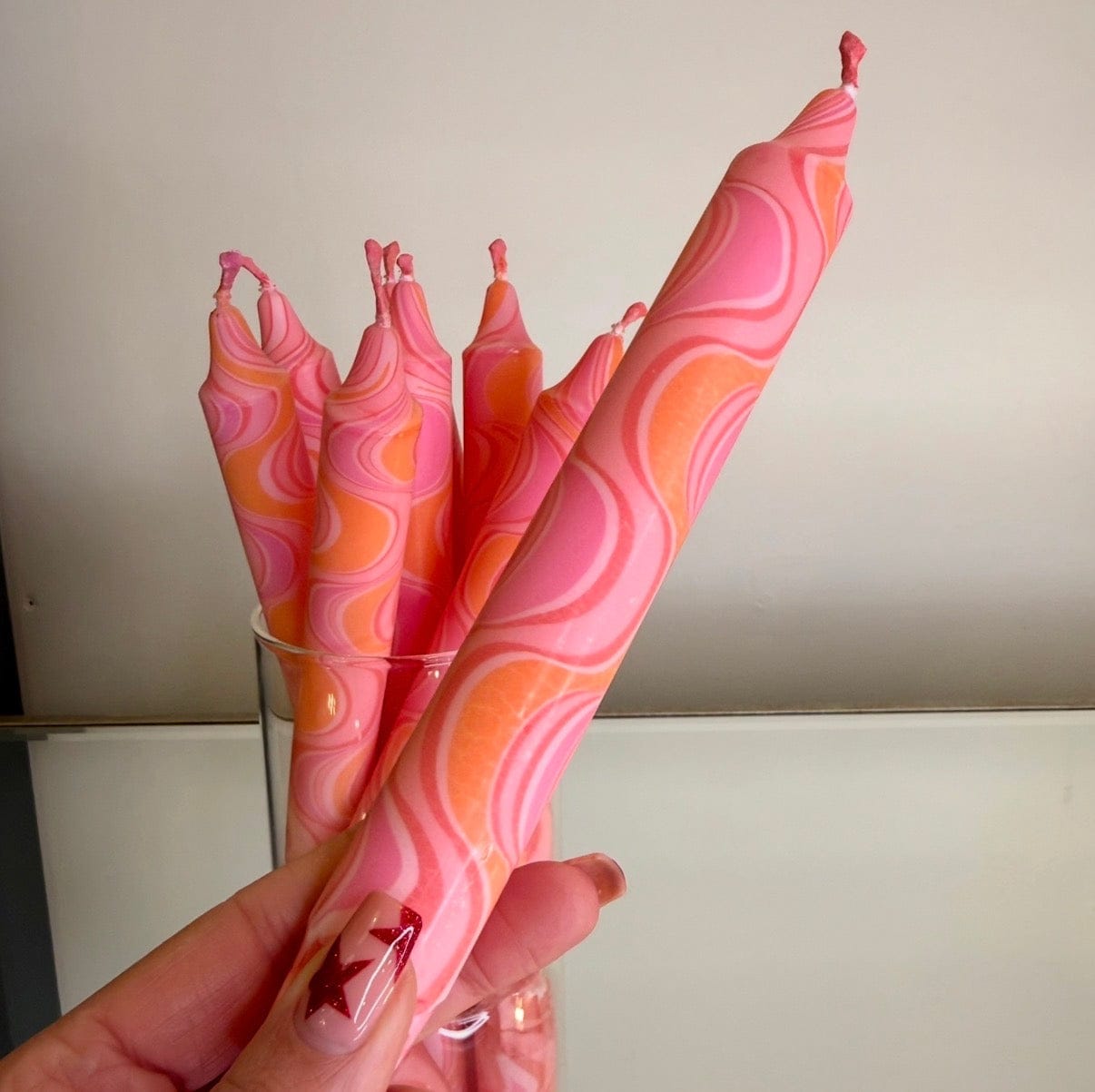 Pink and orange swirled candles held by a hand against a neutral background