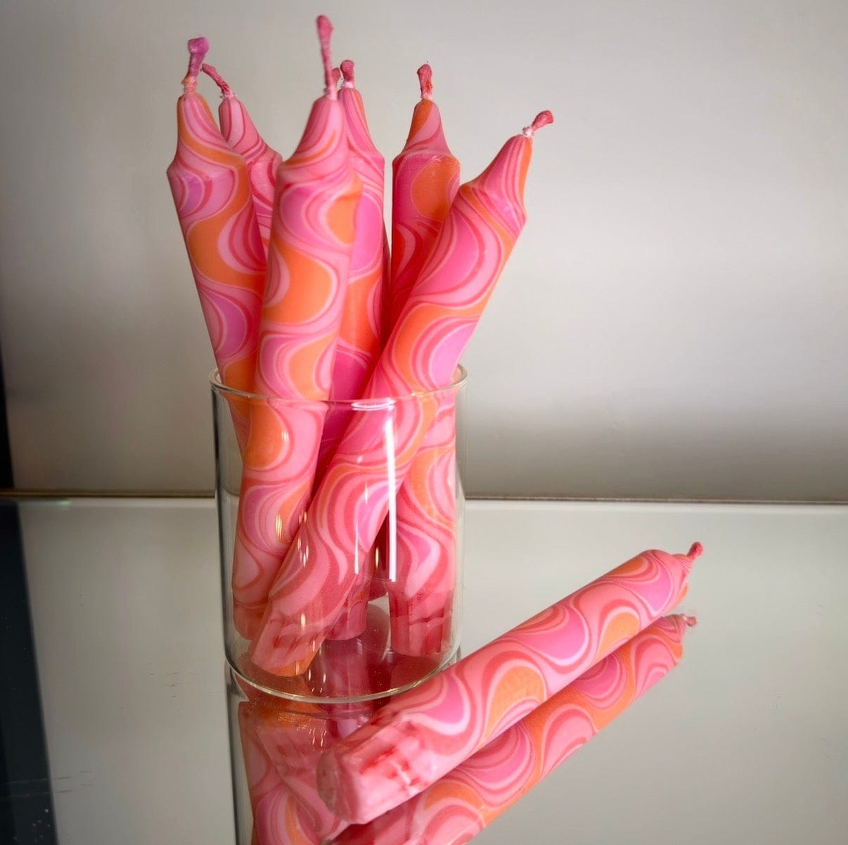 Pink and orange marbled candles in a glass holder on a reflective surface.