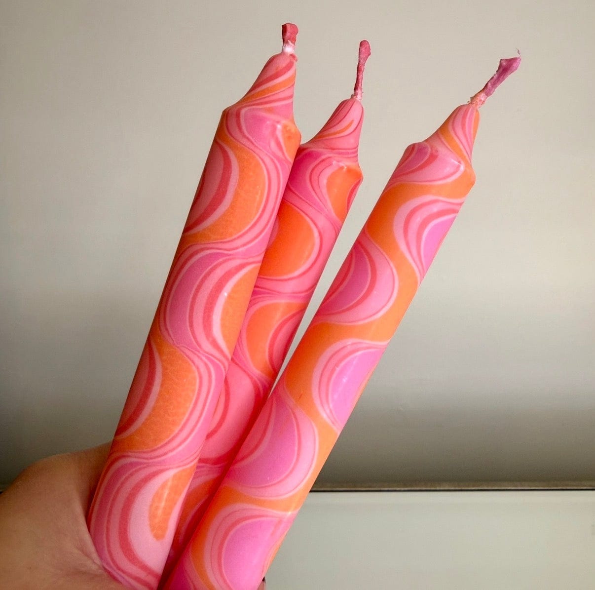 Three pink and orange patterned candles held against a neutral background