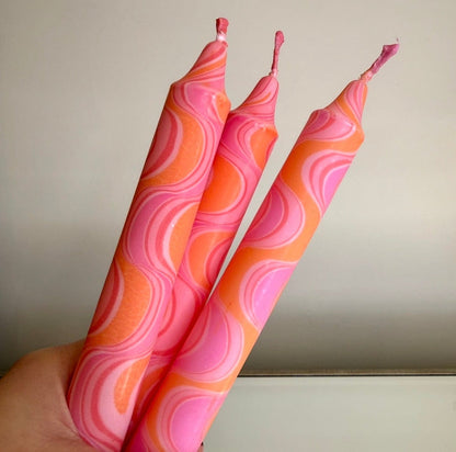Three pink and orange patterned candles held against a neutral background