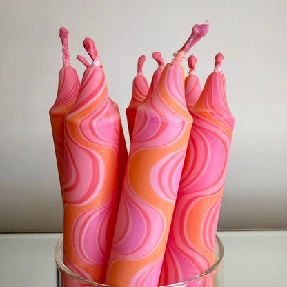Set of pink and orange swirled candles in a glass holder against a plain background
