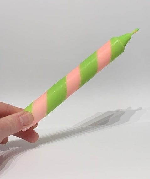 Hand holding a striped pink and green candle against a light gray background