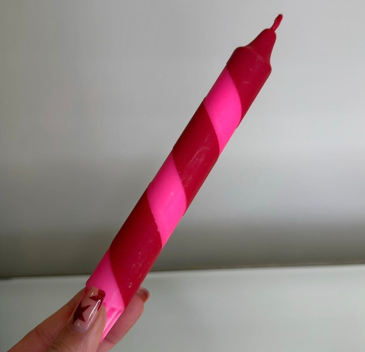 Hand holding a pink and red striped candle against a plain background