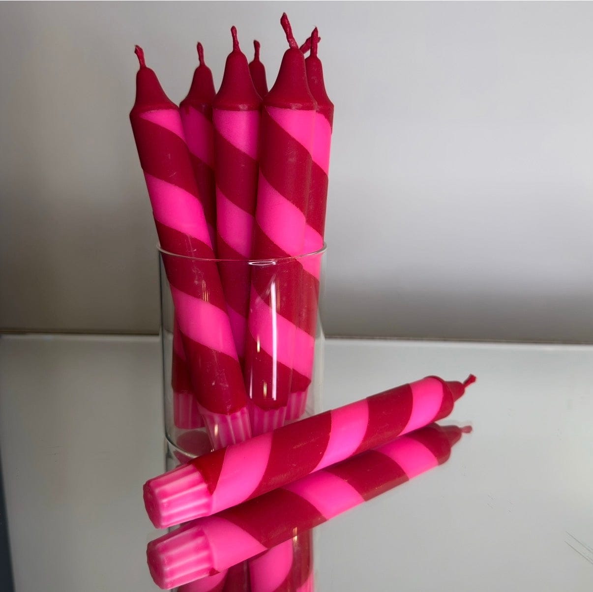 Pink and red striped candles in a clear glass holder on a white surface.