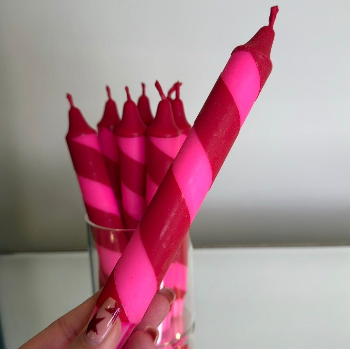 Pink striped candles in a glass holder against a neutral background