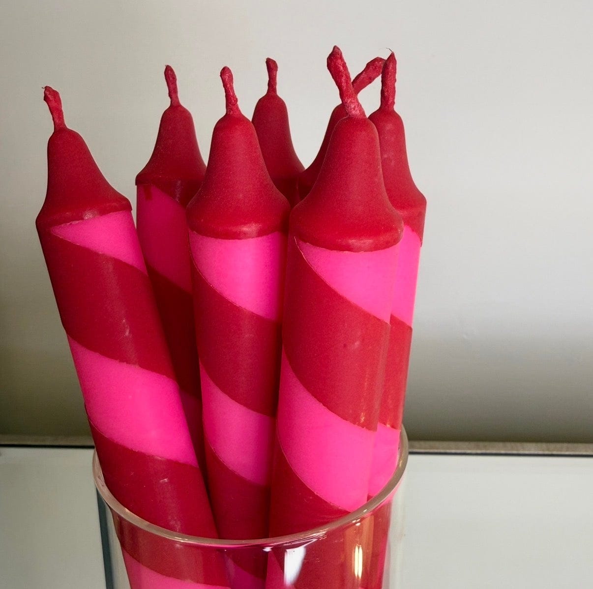 Set of pink and red striped candles in a glass holder against a neutral background