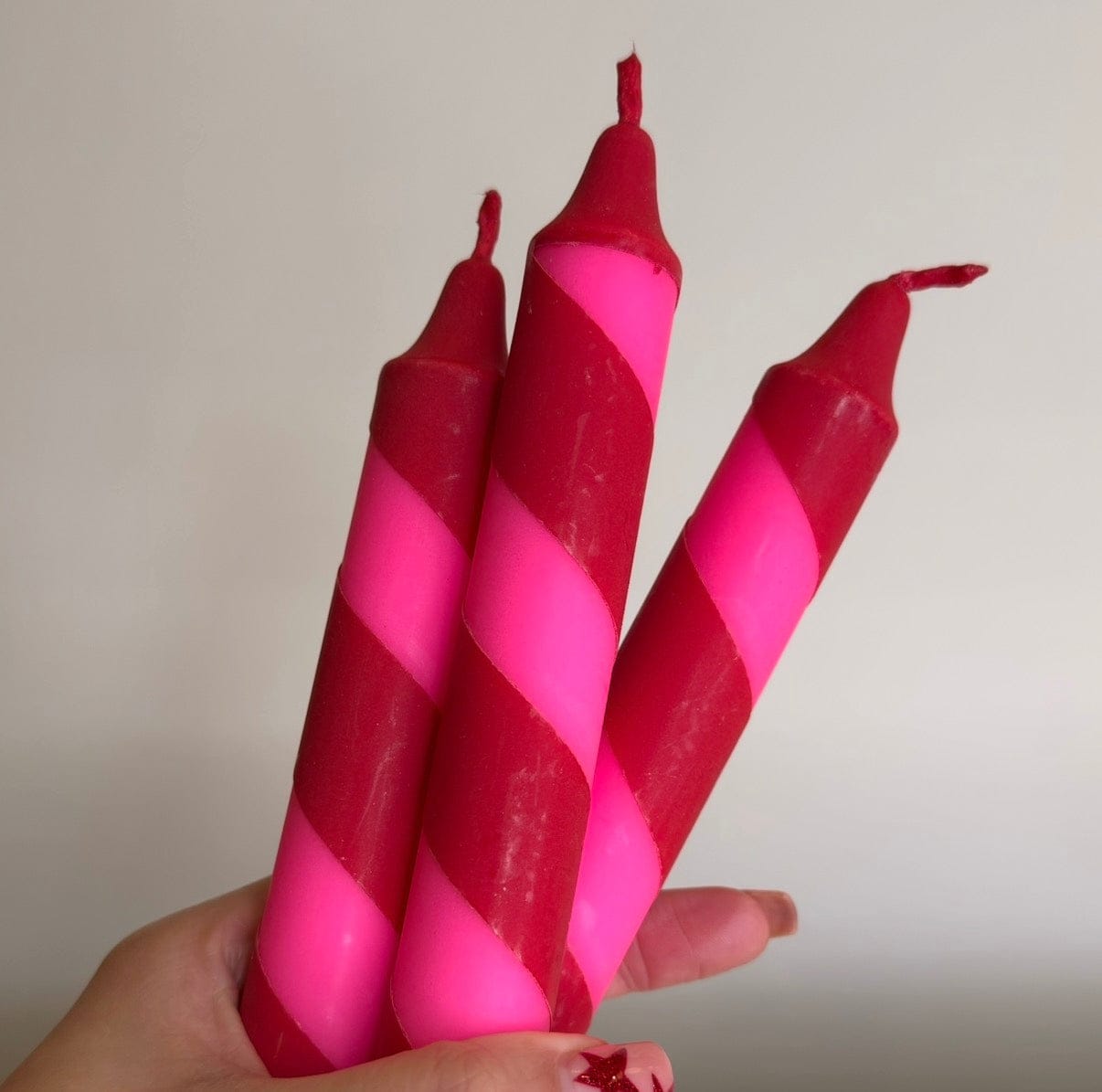 Three pink and red striped candles held in a hand against a plain background