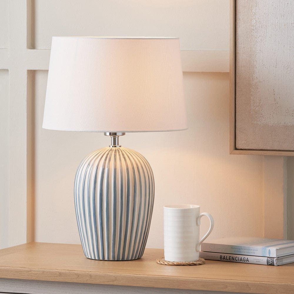 Table lamp with striped design on a wooden surface next to a white mug and books.