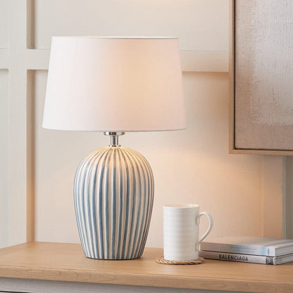 Table lamp with striped design on a wooden surface next to a white mug and books.
