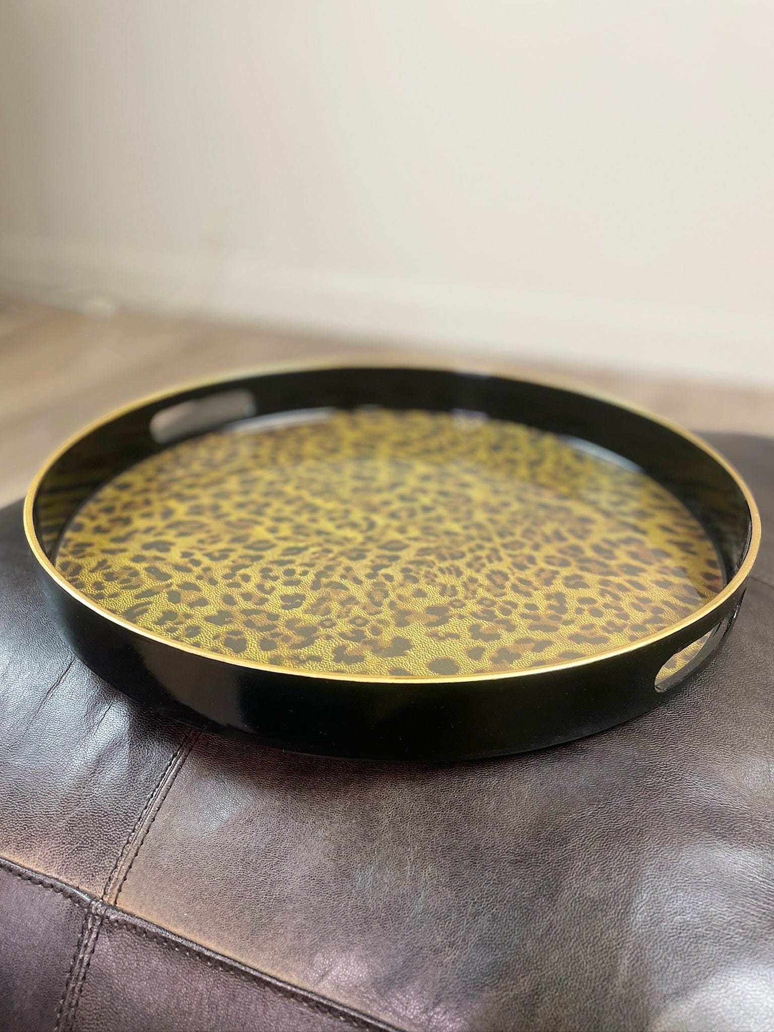 Round black tray with gold leopard print pattern on a leather surface