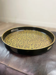 Round black tray with gold leopard print pattern on a leather surface