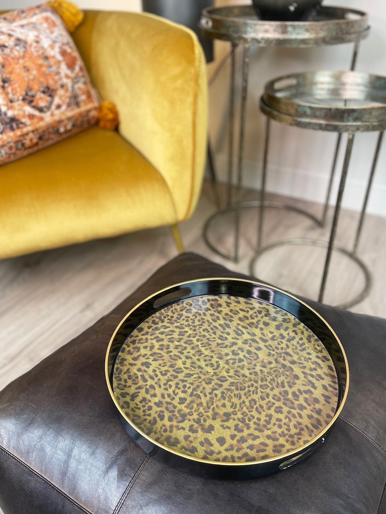 Round decorative tray with leopard print on a dark surface, with a yellow armchair and small table in the background.
