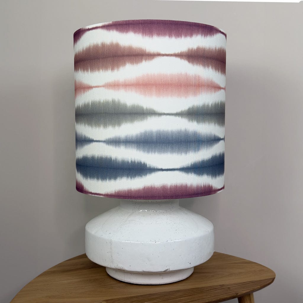 Lamp with a colorful striped shade on a wooden surface against a plain background
