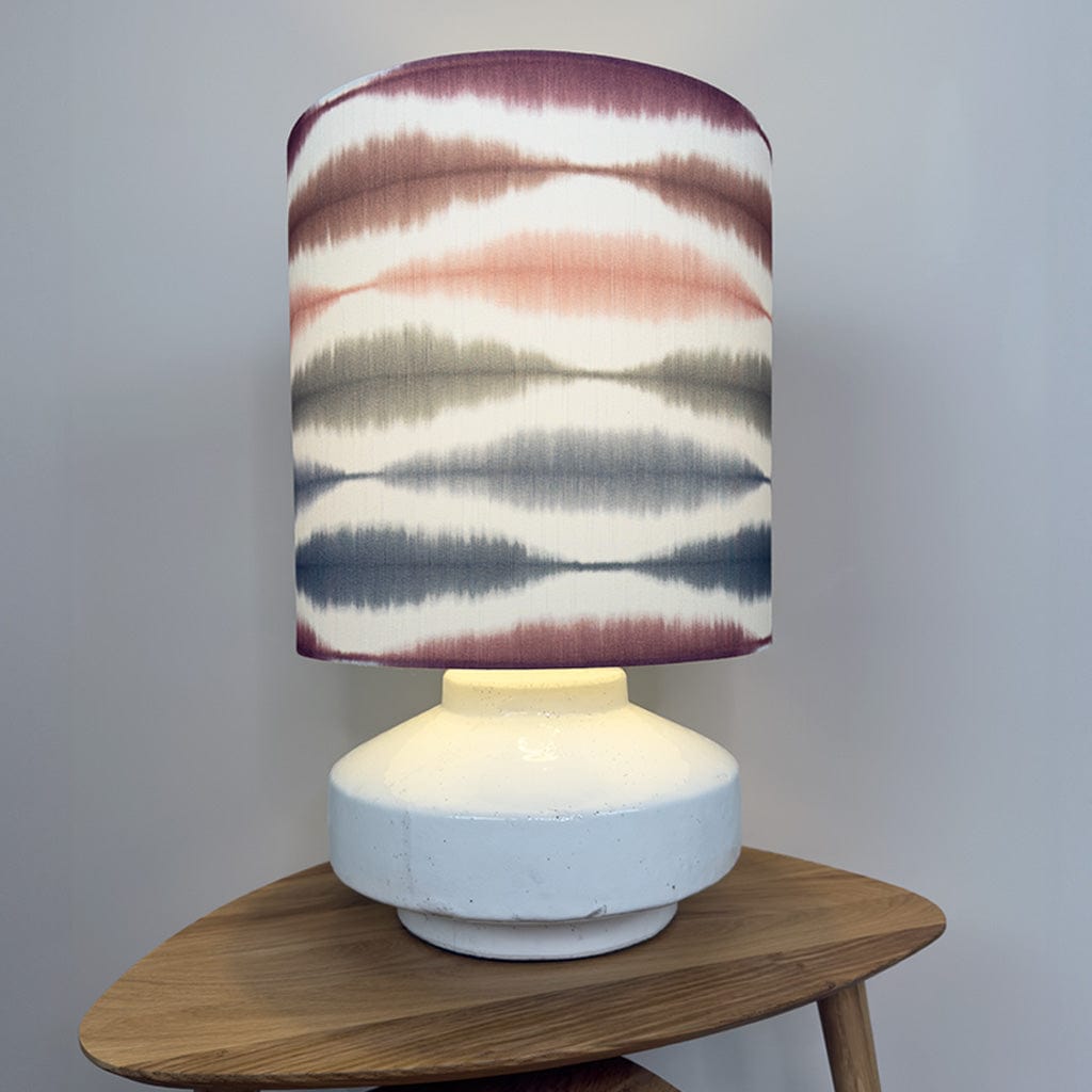 Lamp with a colorful striped shade on a wooden table against a plain background