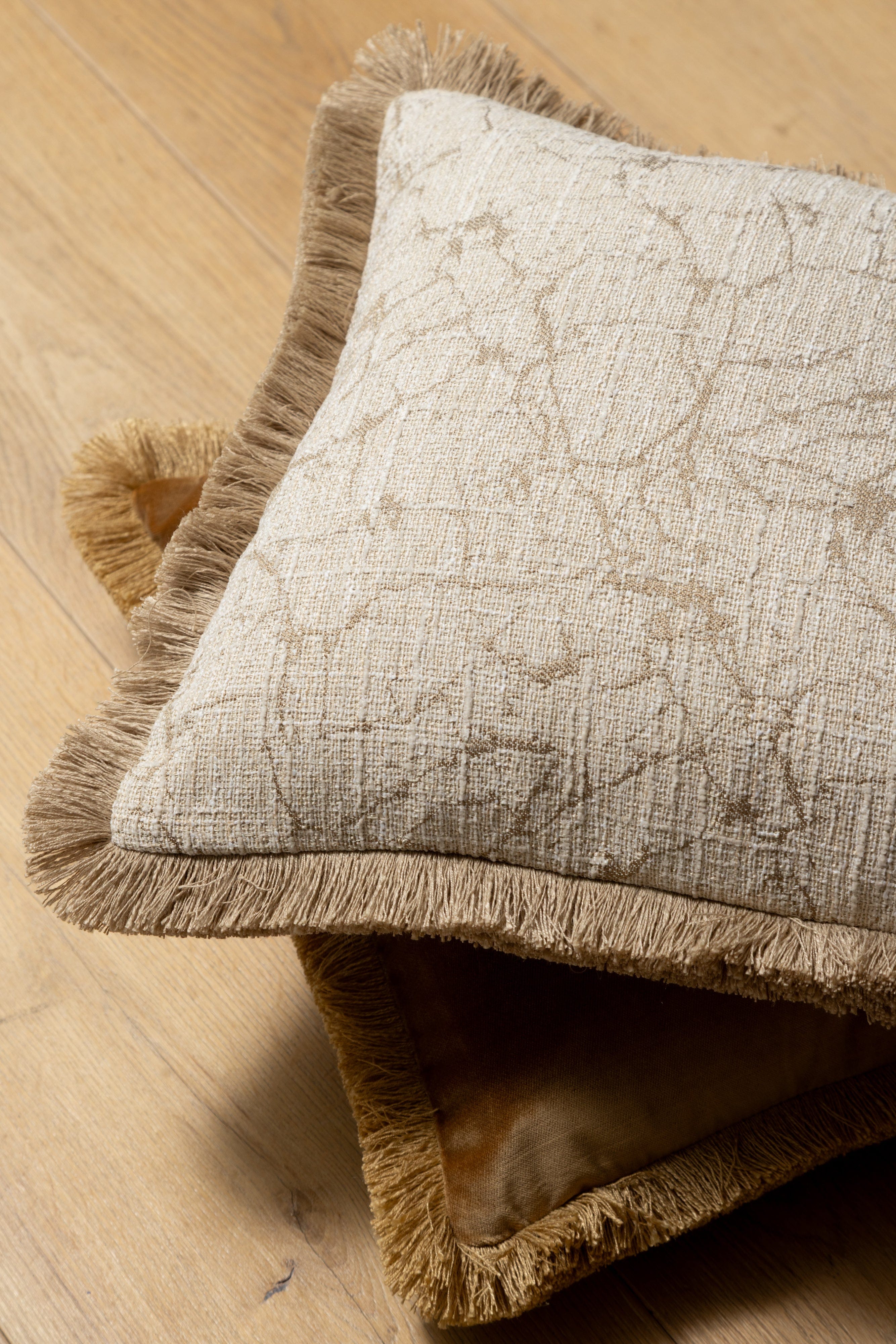 Textured beige gold pillow with frayed edges on a wooden surface