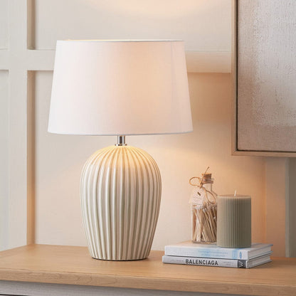 Decorative lamp with ribbed ceramic base on a shelf with books and a candle.