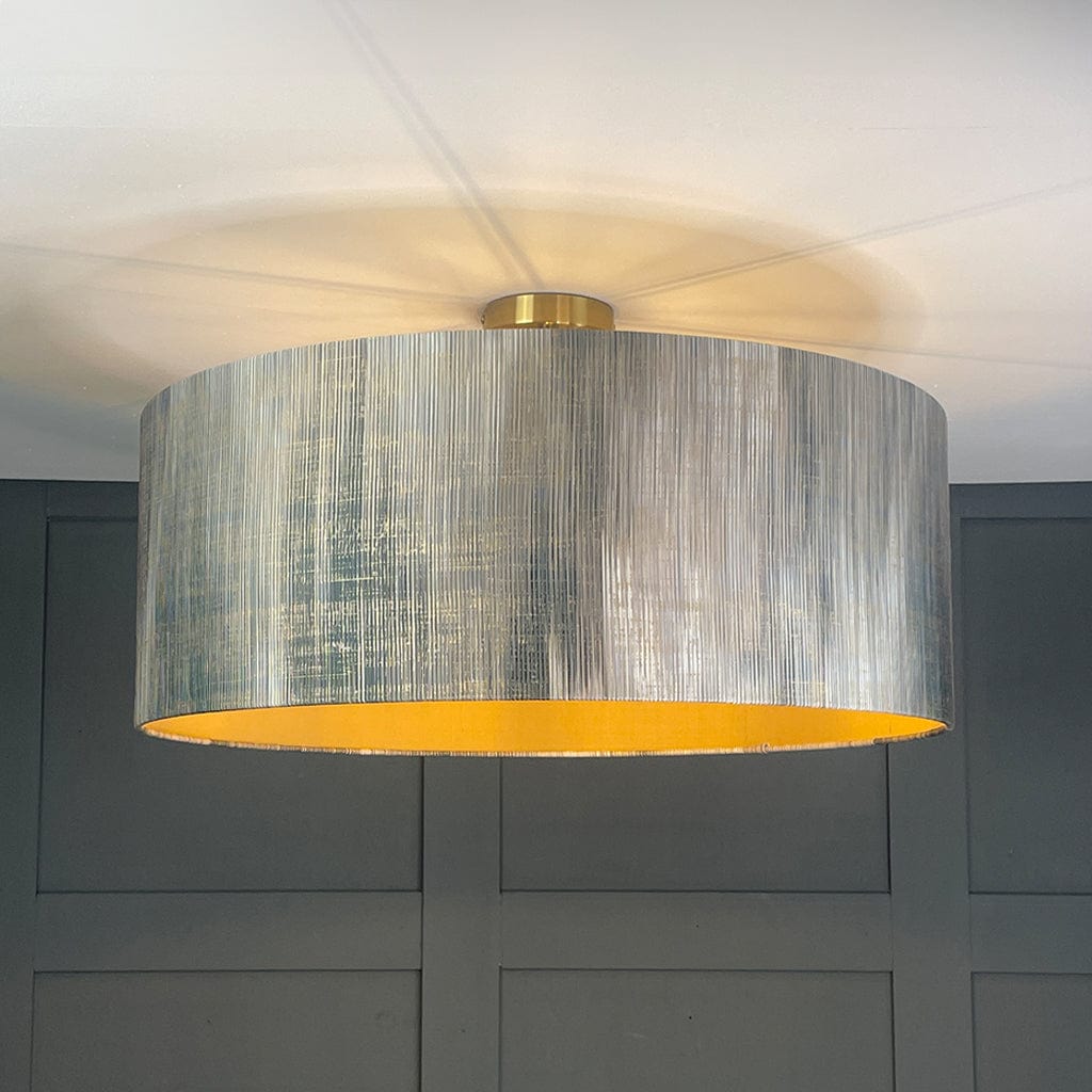 Ceiling light fixture with a textured gray shade and gold trim against a dark gray wall.