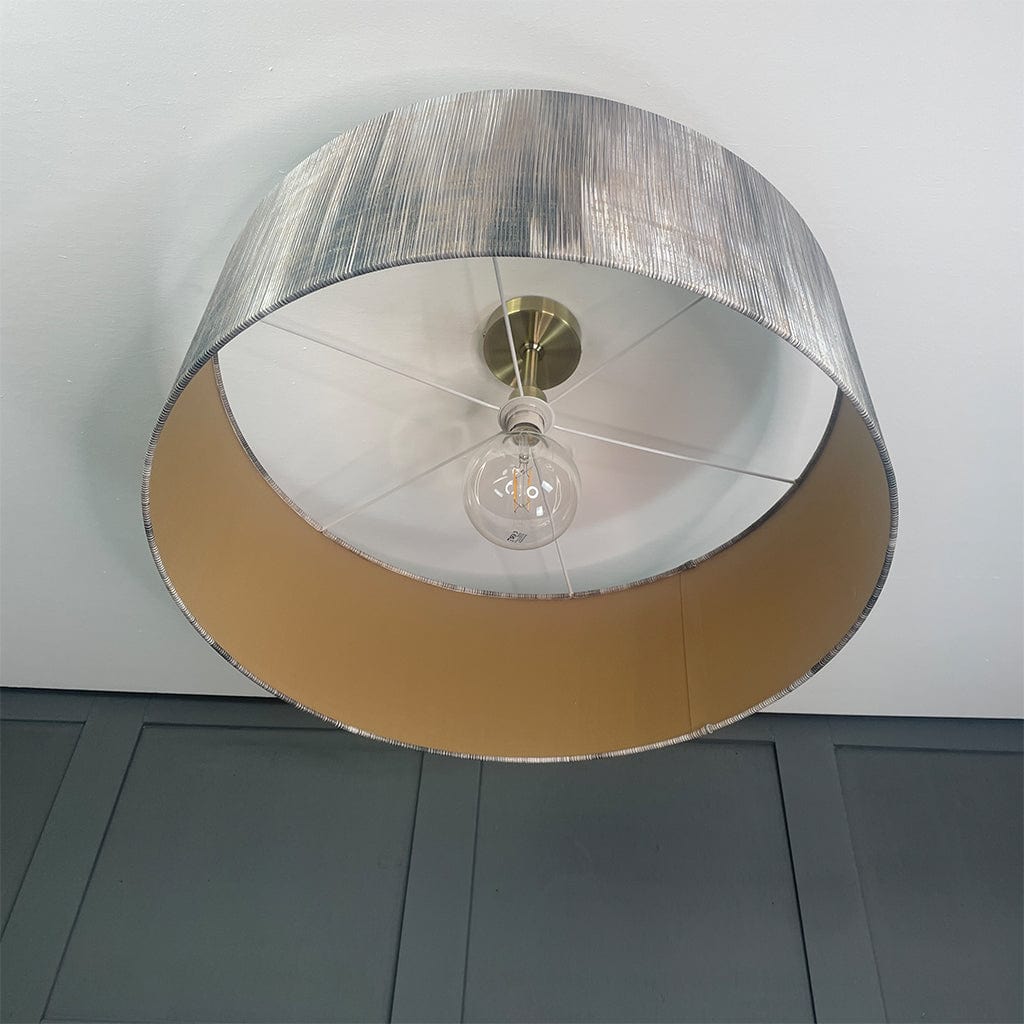 Ceiling light fixture with metallic shade and visible bulb against a gray wall.