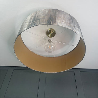 Ceiling light fixture with metallic shade and visible bulb against a gray wall.