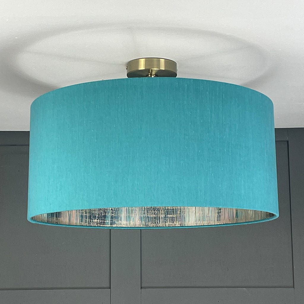 Turquoise ceiling light fixture with gold fitting against a gray wall.