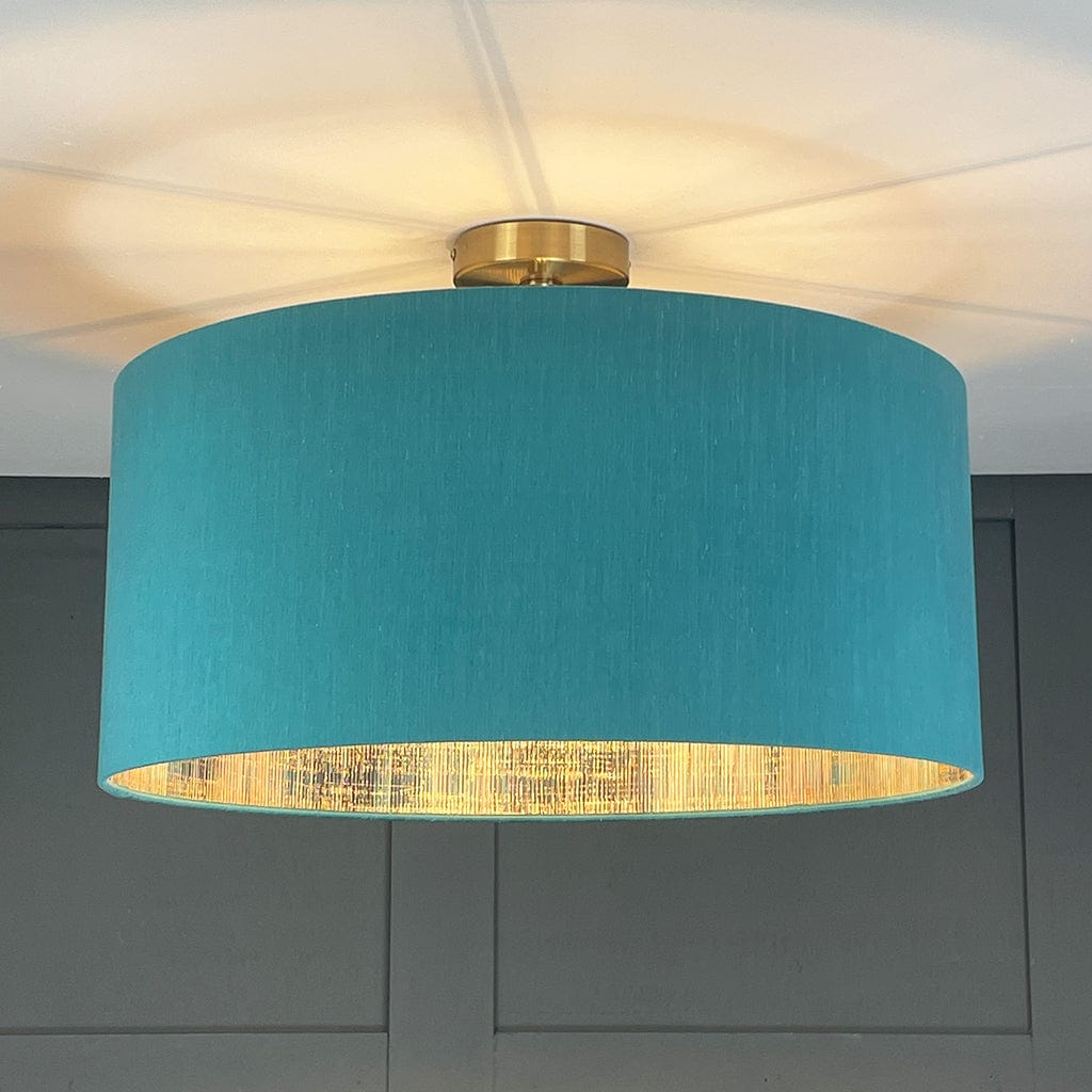 Ceiling light fixture with teal shade and gold inner lining against a neutral wall.