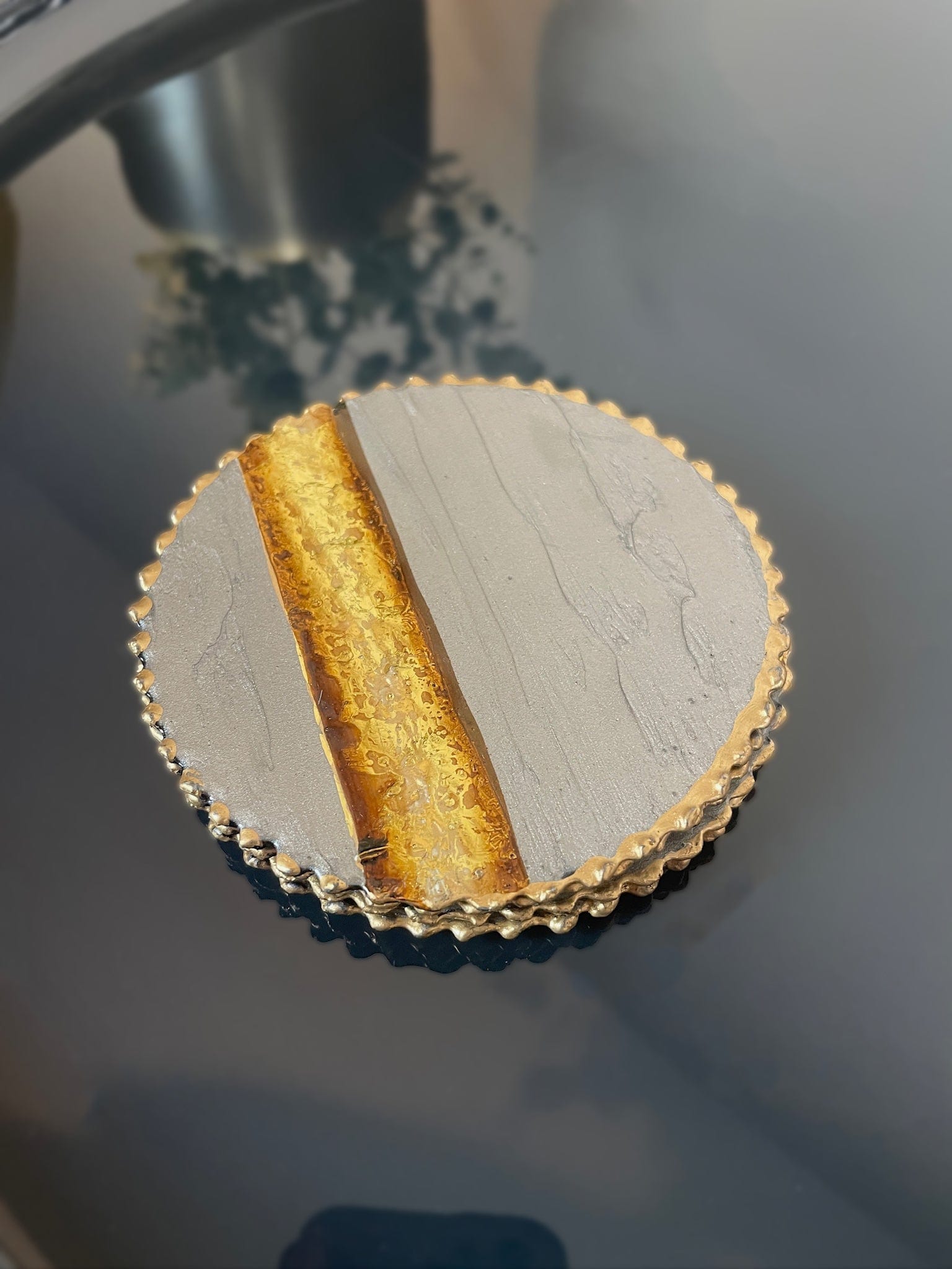 Close-up of a decorative coaster with gold edge on a reflective surface