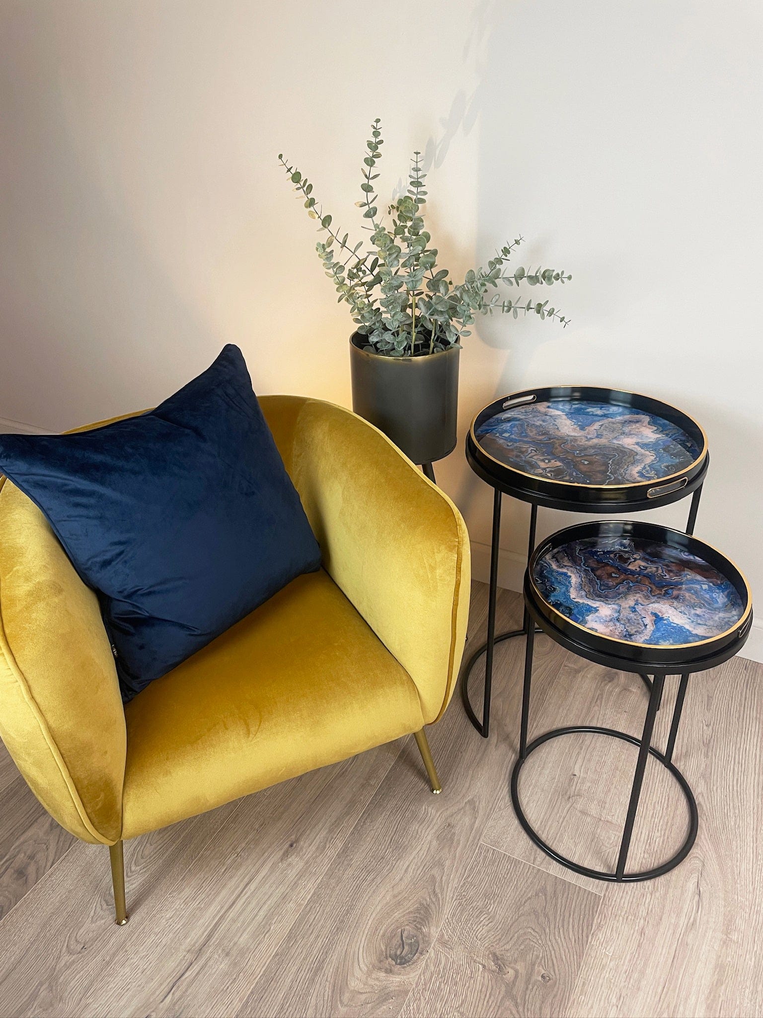 Yellow armchair with a blue pillow and two decorative side tables with blue marble design on a wooden floor.