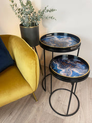 Two round black tables with marble-like blue and gold designs next to a yellow armchair.