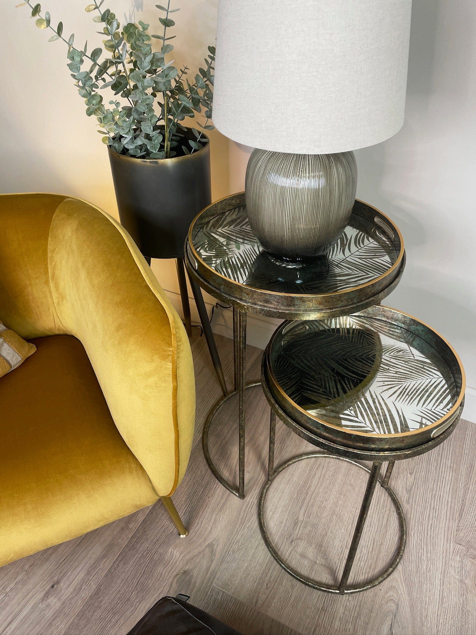 Gold armchair next to a small round table with a lamp and plant in a room.
