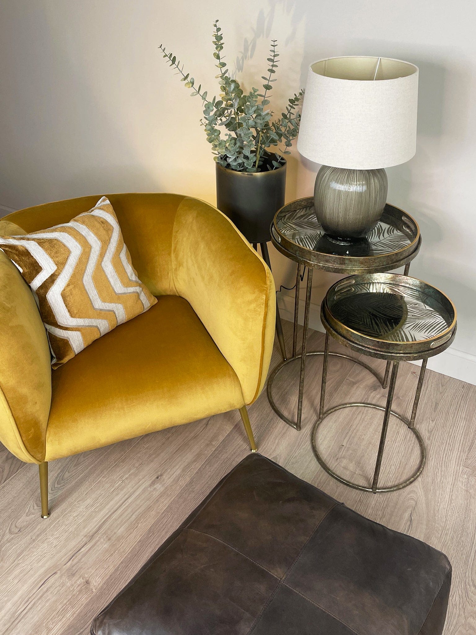 Yellow armchair with a patterned pillow, side table with lamp, and small round table in a room.
