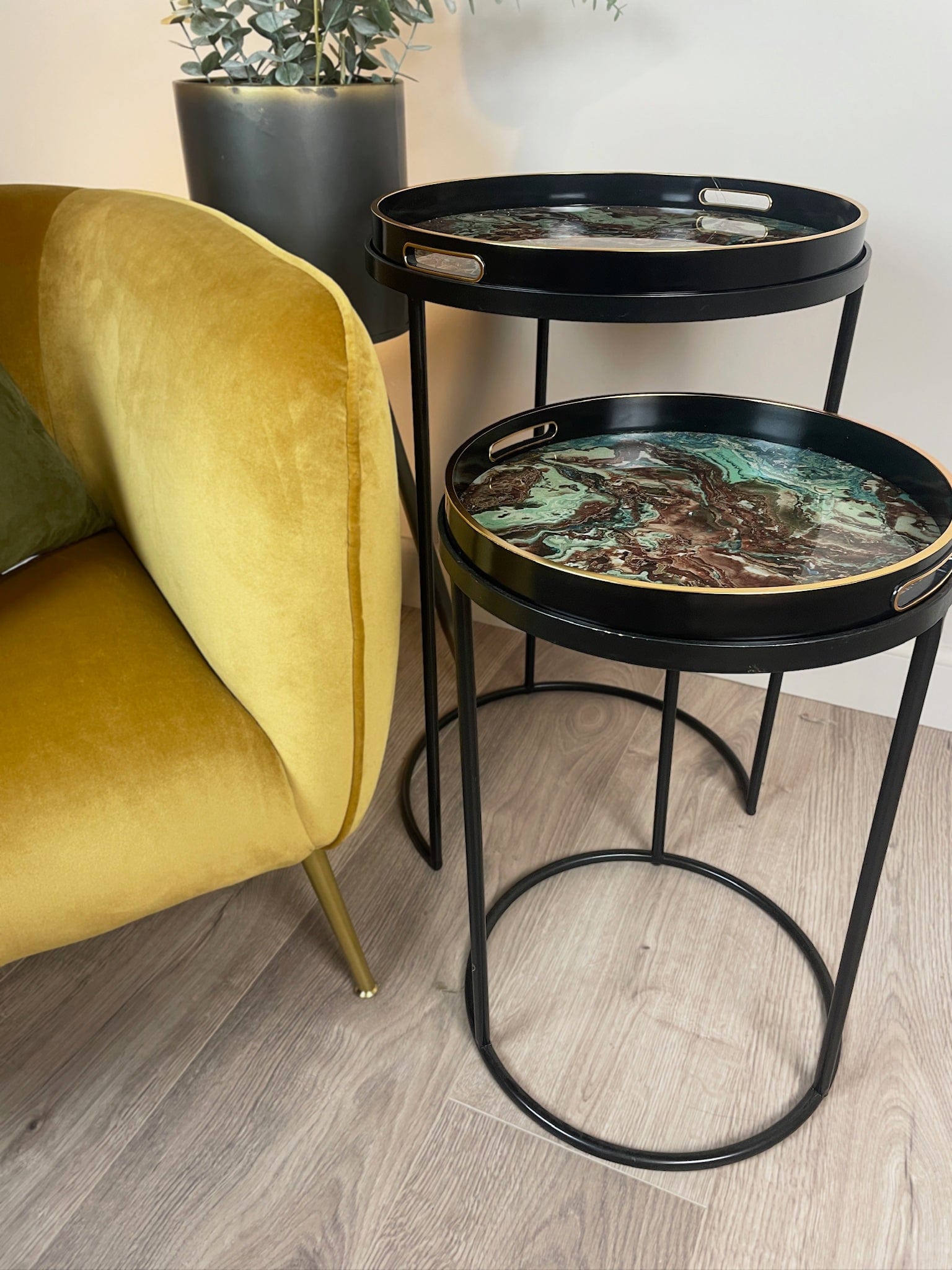 Black metal side table with decorative trays next to a yellow armchair.