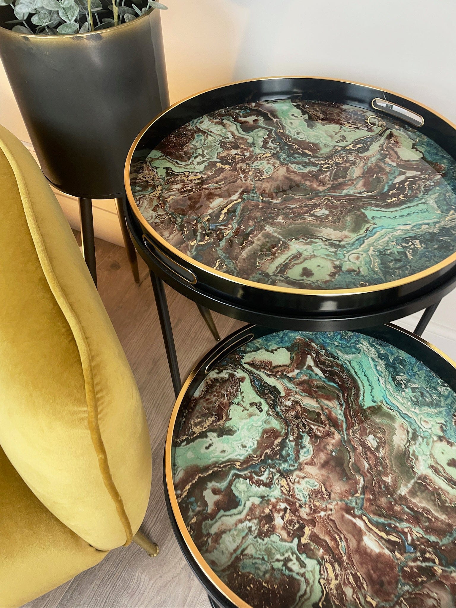 Two round marble-patterned tables with gold edges in a room setting.