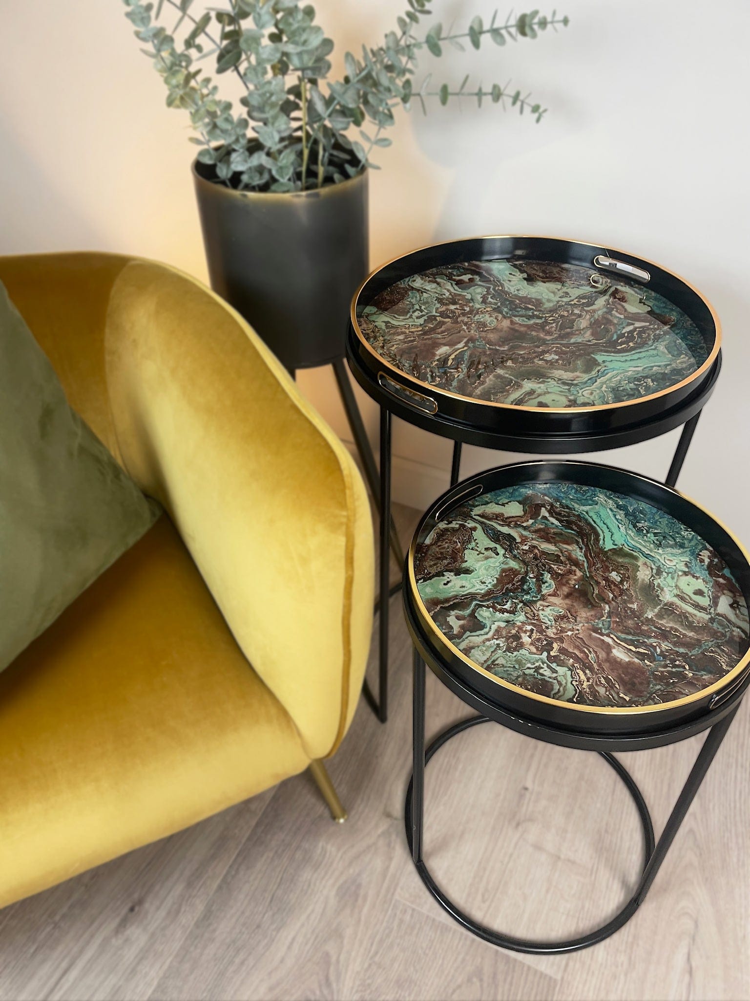 Two round marble-top side tables with black metal frames next to a yellow chair and a potted plant.