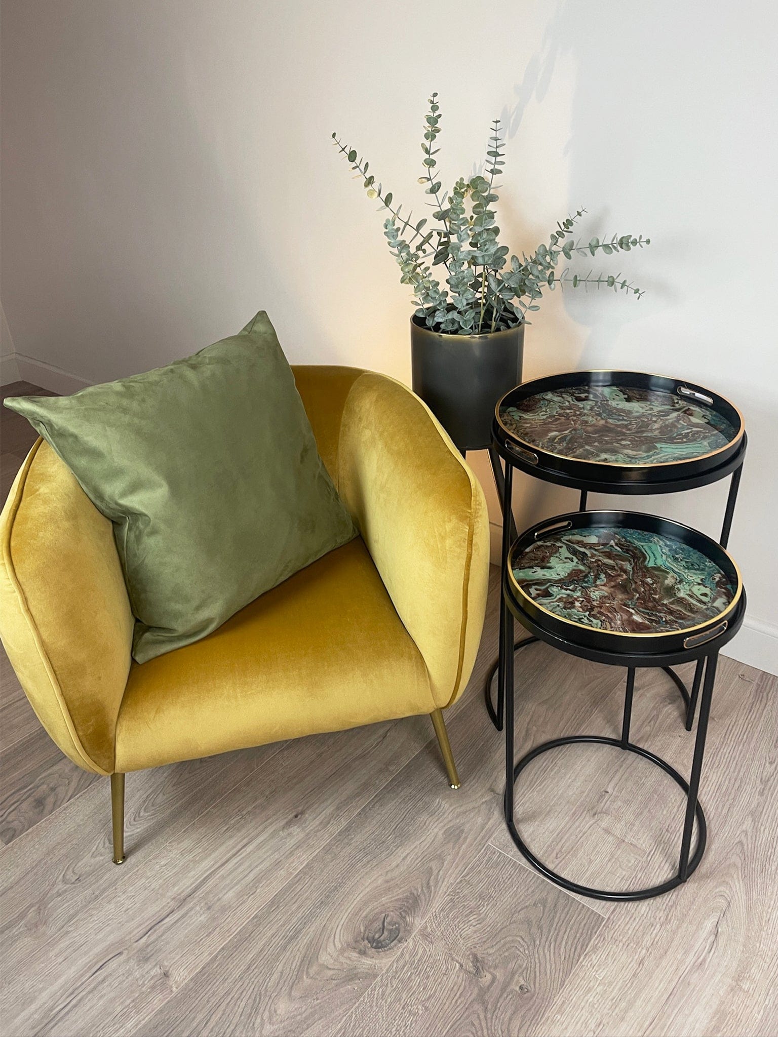 Yellow armchair with a green pillow, black side table with decorative items, and potted plant in a room.