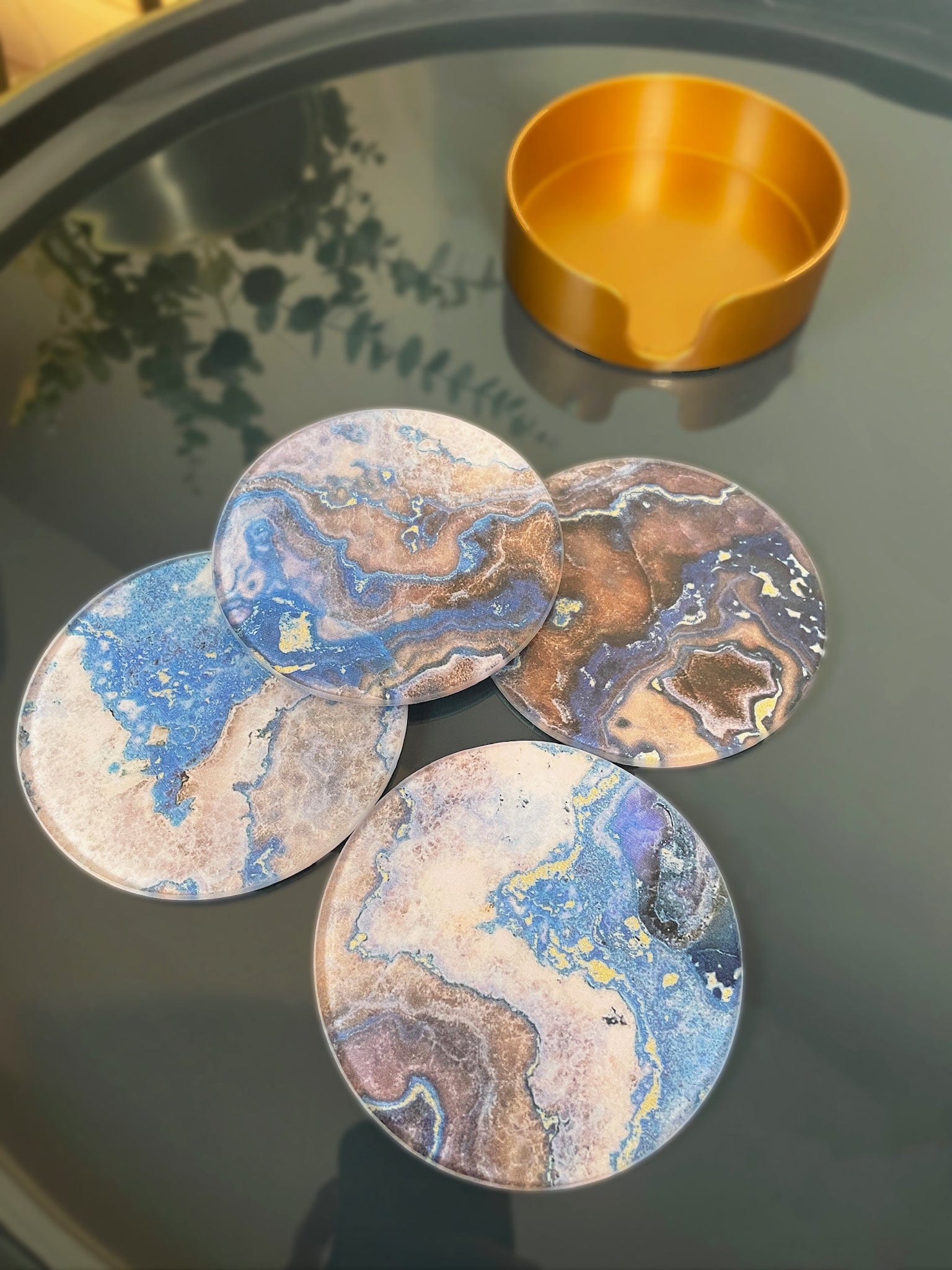 Marble-patterned coasters on a reflective surface with a gold container.