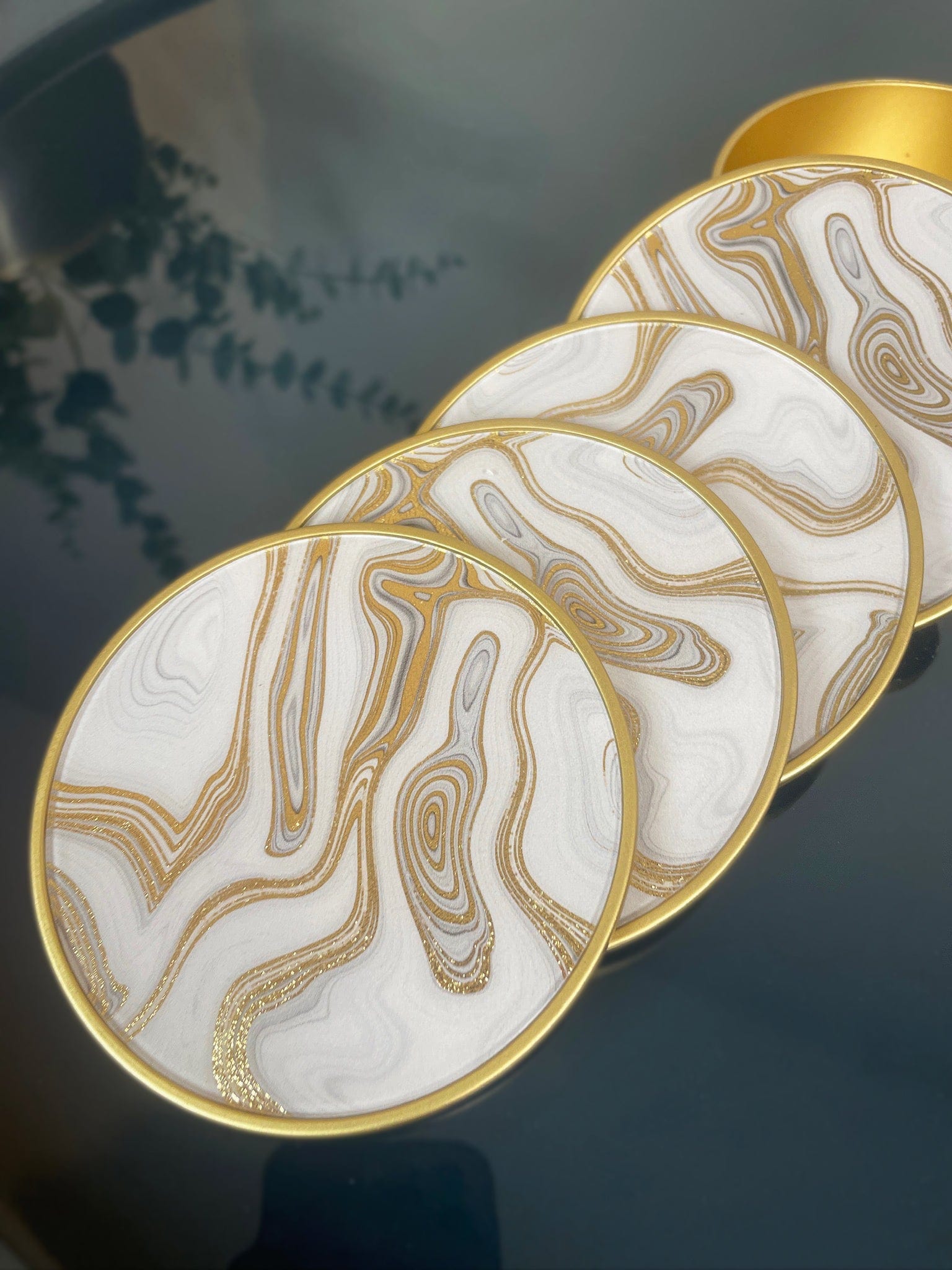Set of four decorative coasters with marble-like design and gold edges on a dark surface.