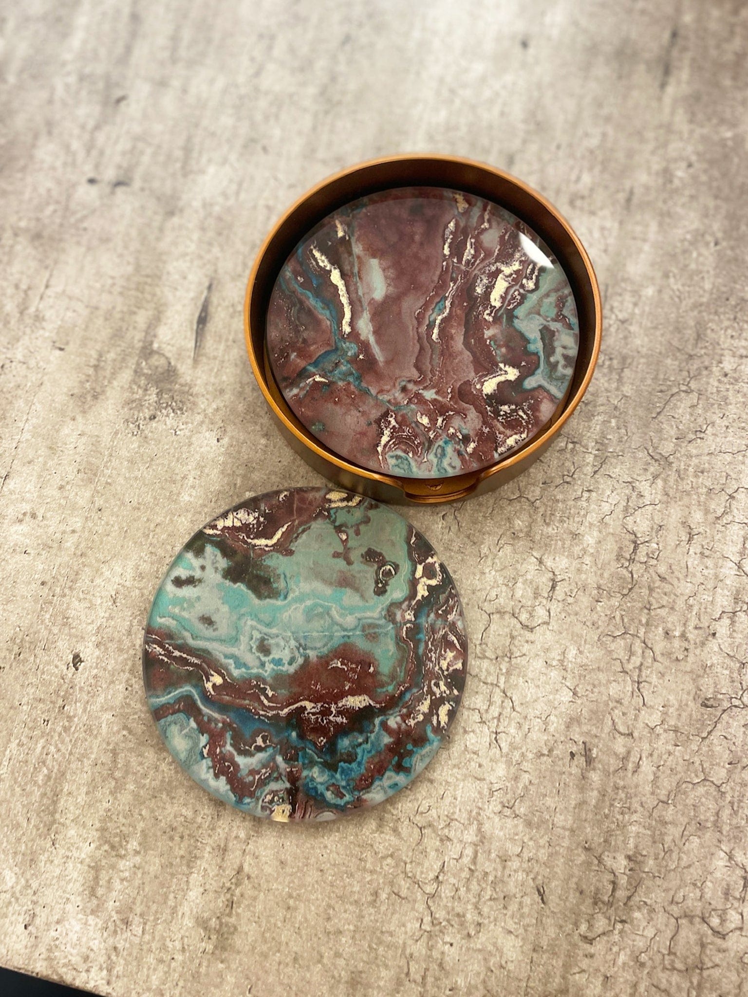 Marbled glass coasters in a bronze container on a textured surface