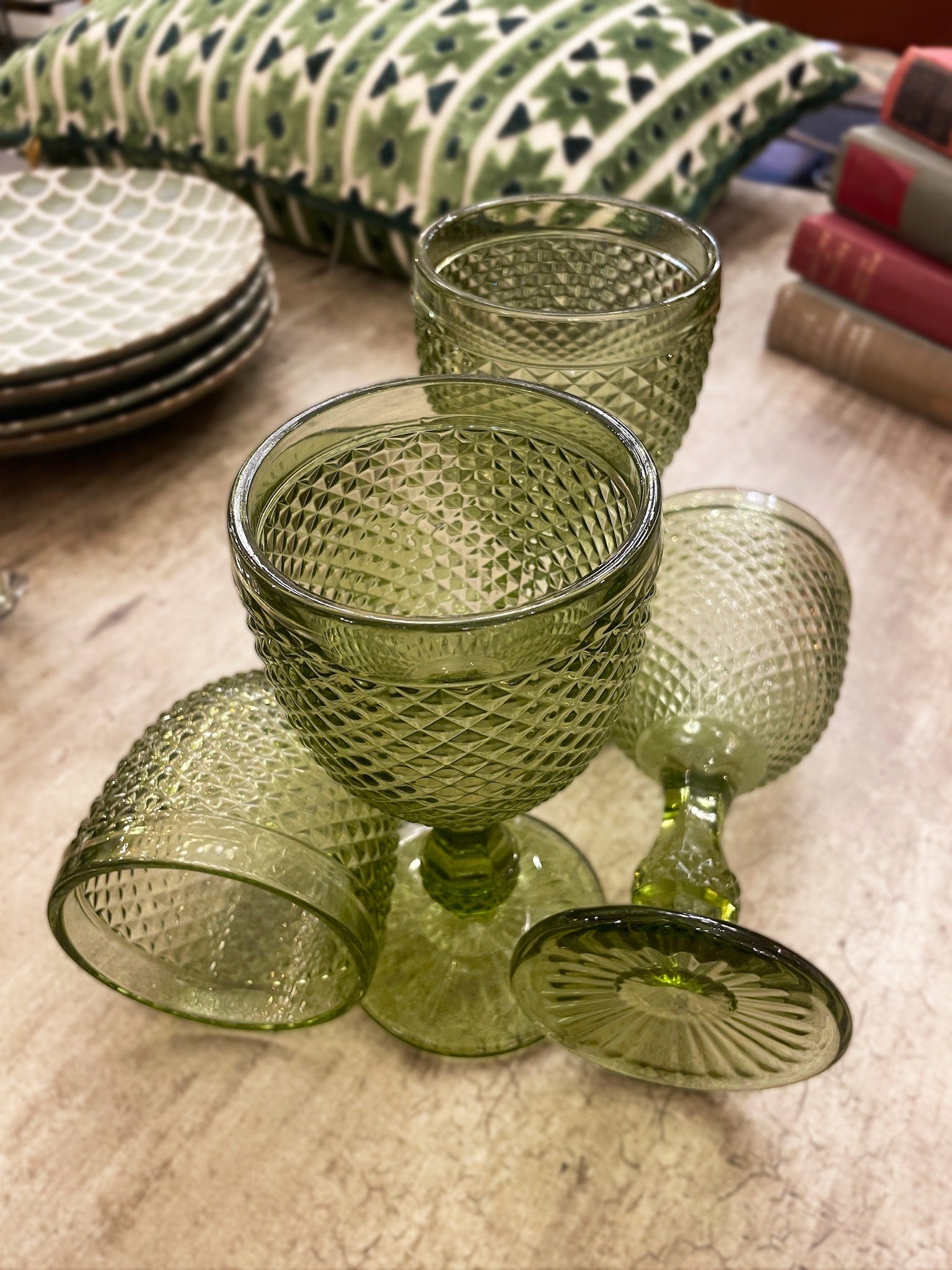Set of green glass goblets on a textured surface with books and a pillow in the background.
